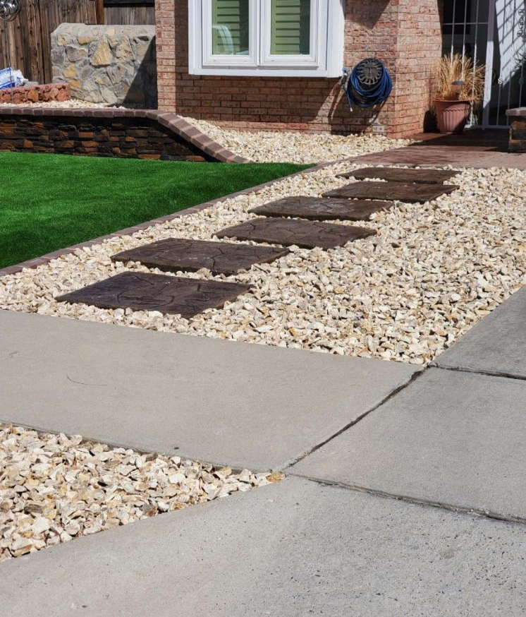 Stone pathway with stepping stones and gravel beside green grass and a brick house.