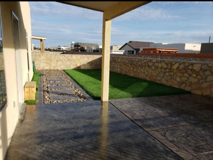 Patio with a stone wall, green grass, and concrete path.