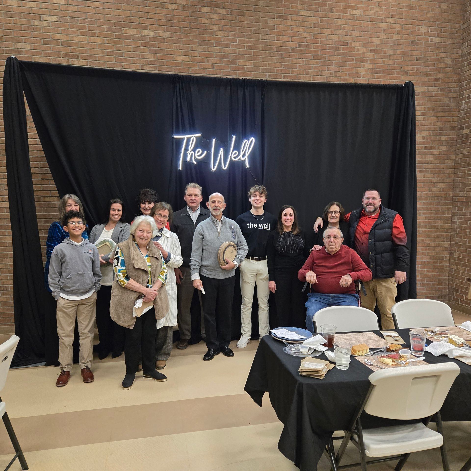 A group of people poses for a photo in front of a black curtain with a neon sign reading