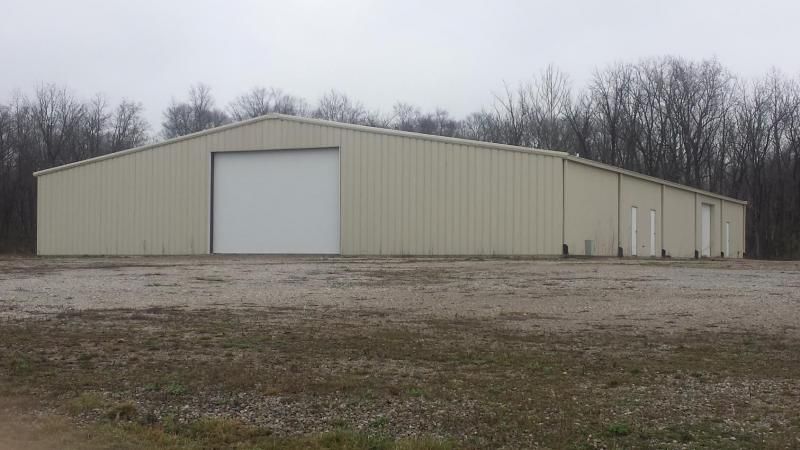 A tan metal warehouse building with a large garage door, set in a rural area.