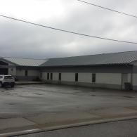 Building with a metal roof and several windows on a cloudy day. A vehicle is parked in front.