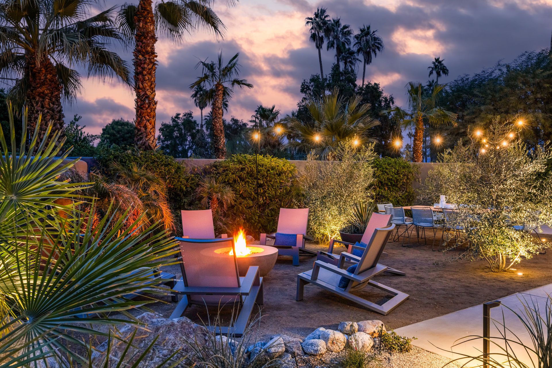 Fire pit area at dusk with chairs, string lights, and desert plants.