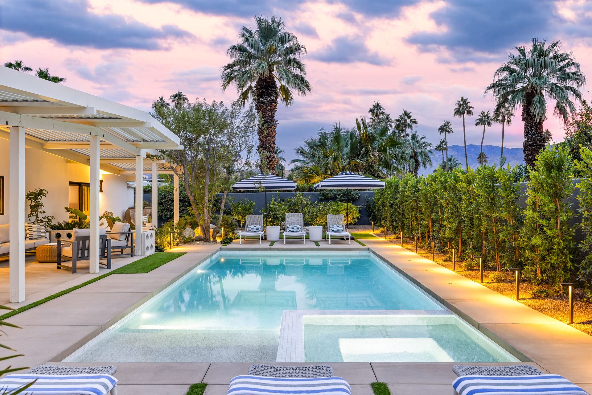 Rectangular pool with lounge chairs, palm trees, and a covered patio at sunset.
