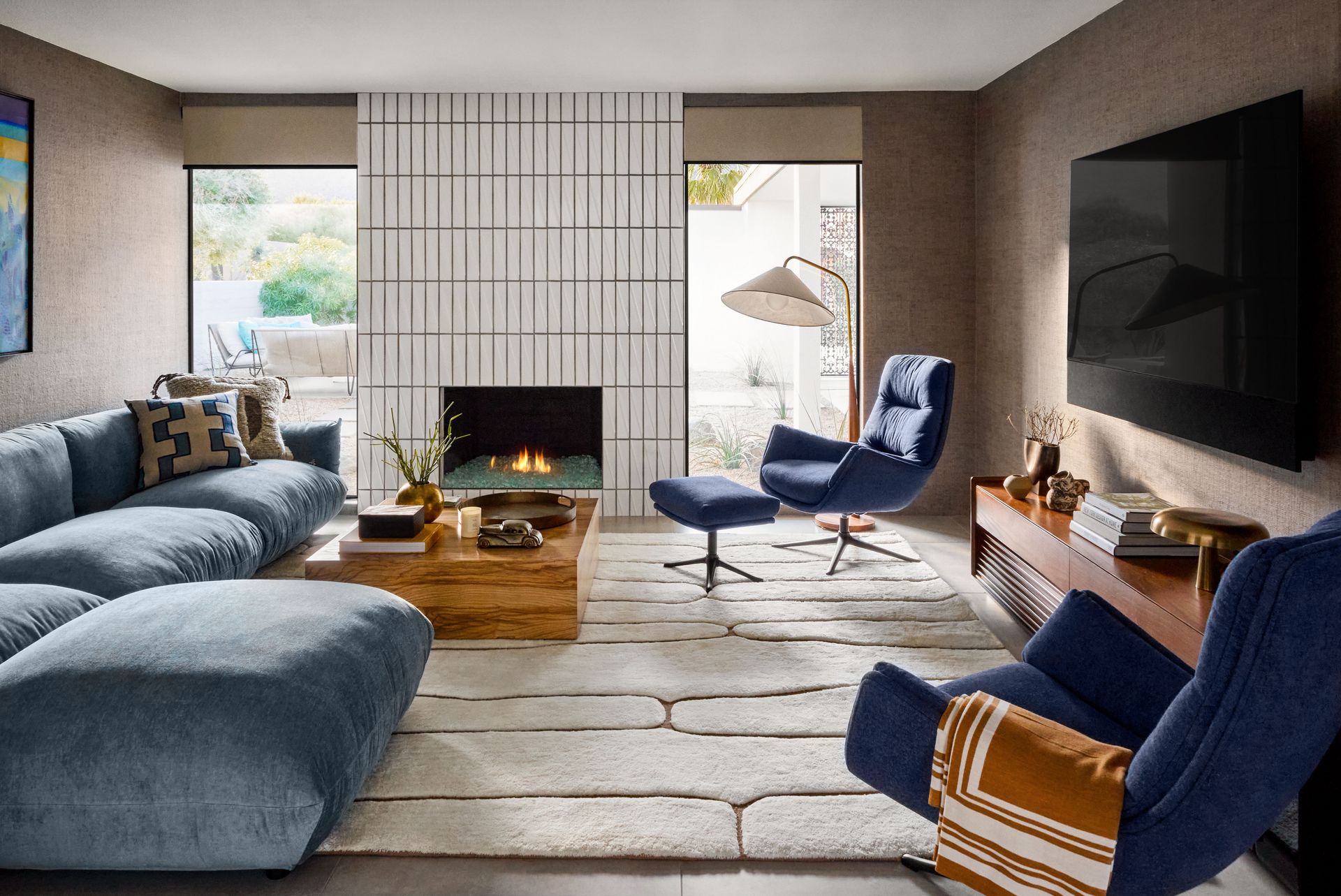 A living room with a blue couch , blue chairs , a fireplace and a flat screen tv.