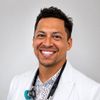 Smiling doctor in white coat with stethoscope against a light gray background