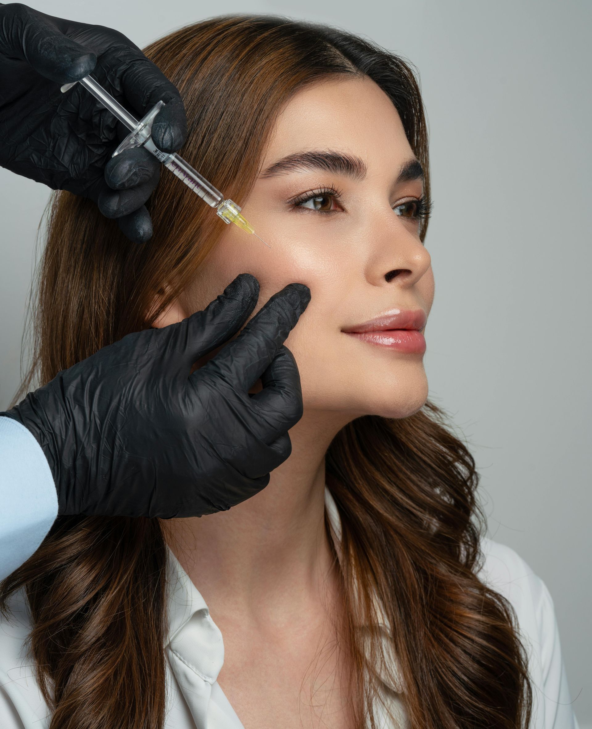 Gloved hands inject a woman’s cheek with a syringe in a clinical setting.