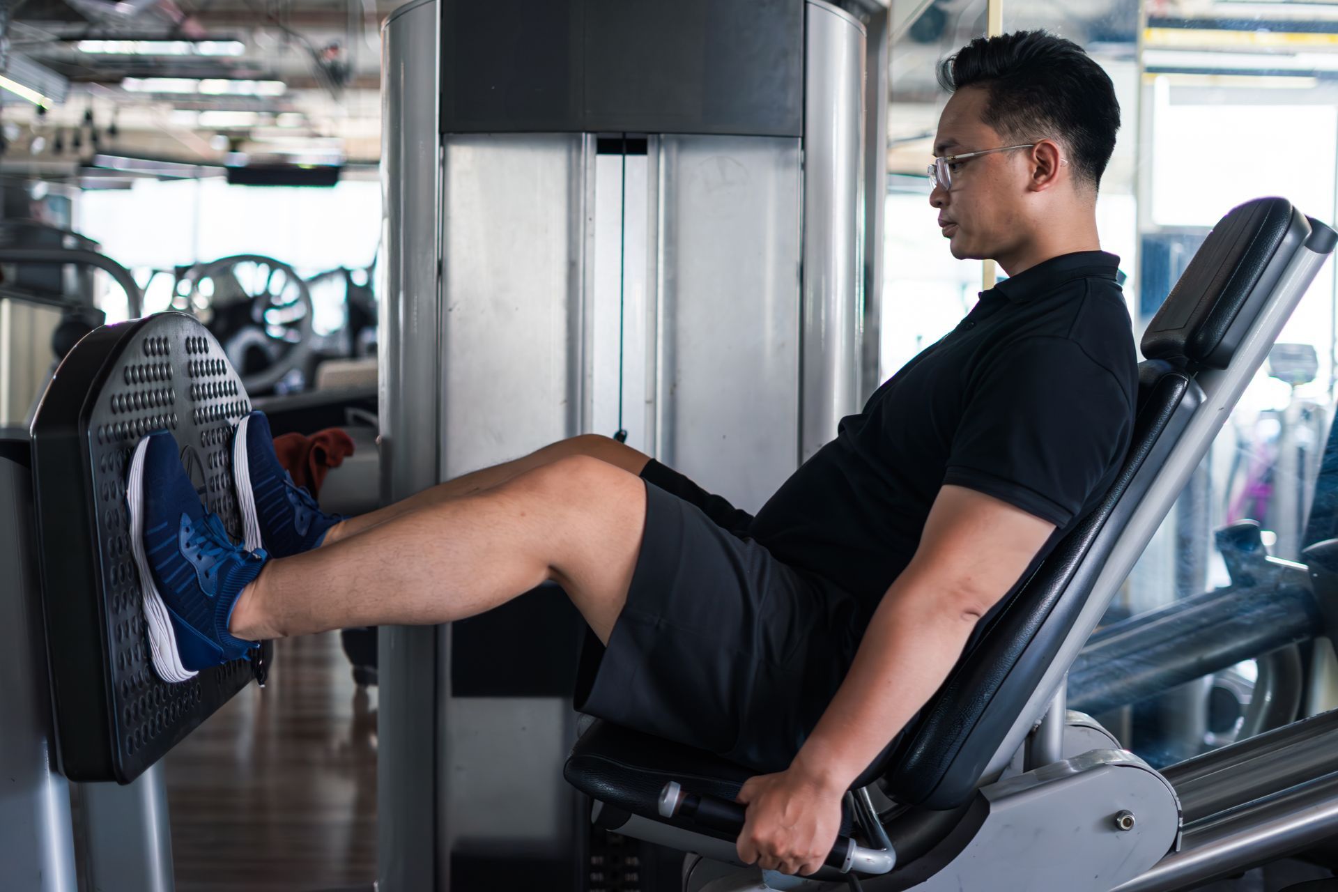 Man using a leg press machine at a gym, wearing black shirt and shorts.