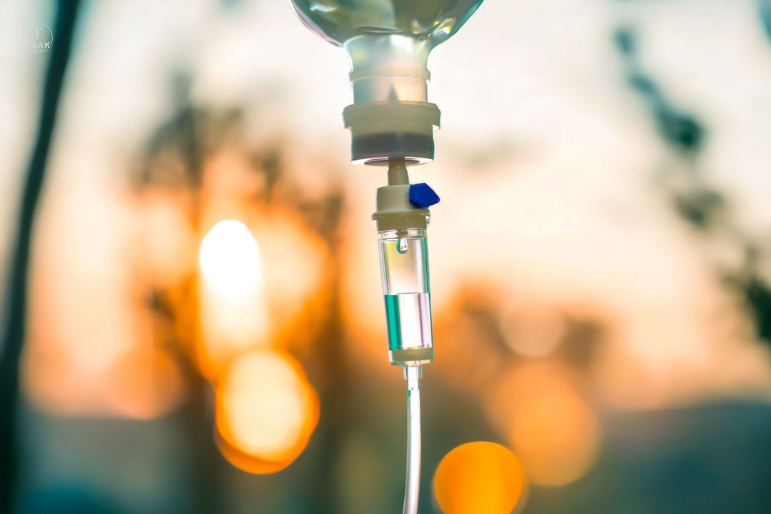 IV drip, clear fluids flowing from bag into tubing, blurred background.