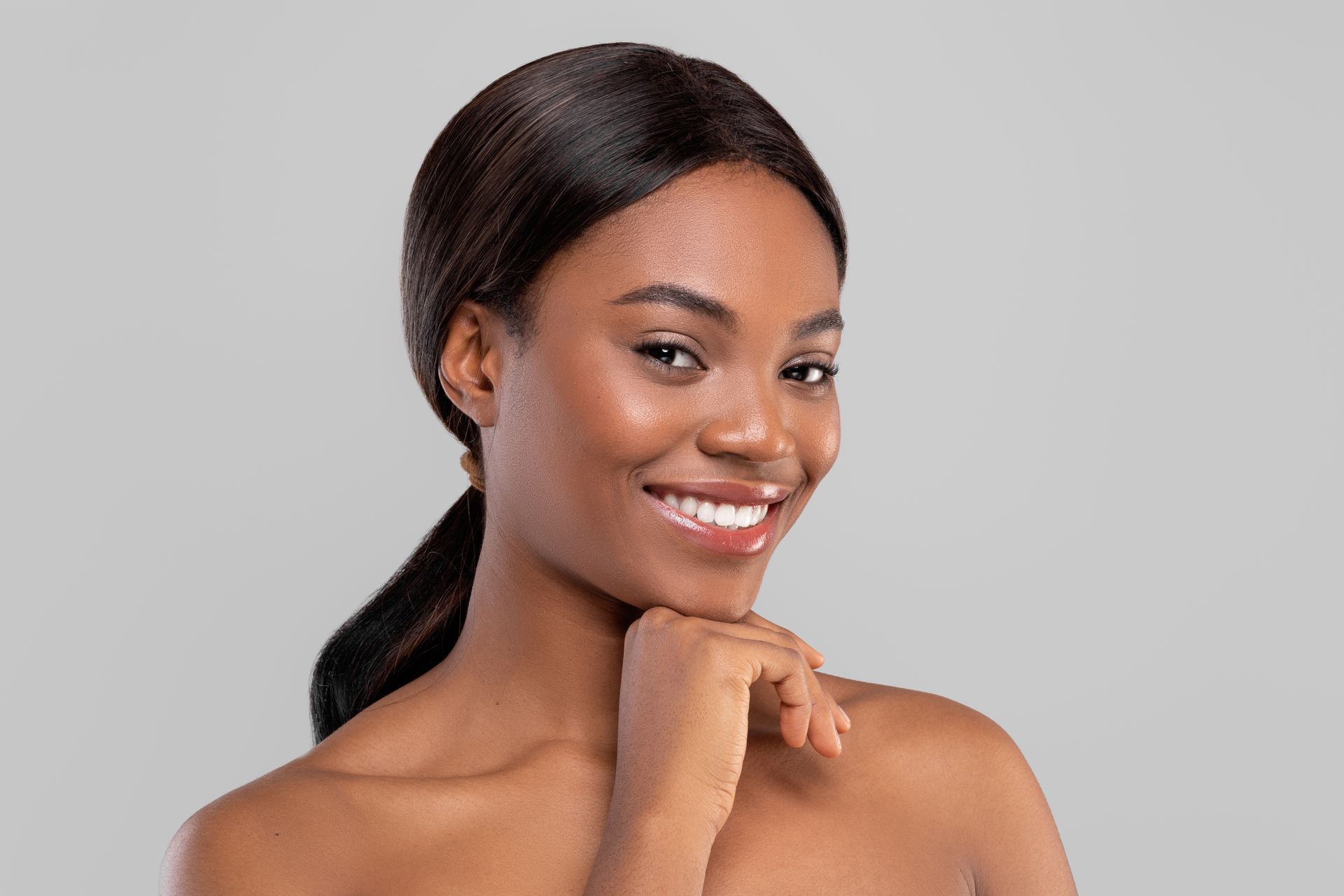 Woman with dark hair smiling, hand under chin, against a gray background.