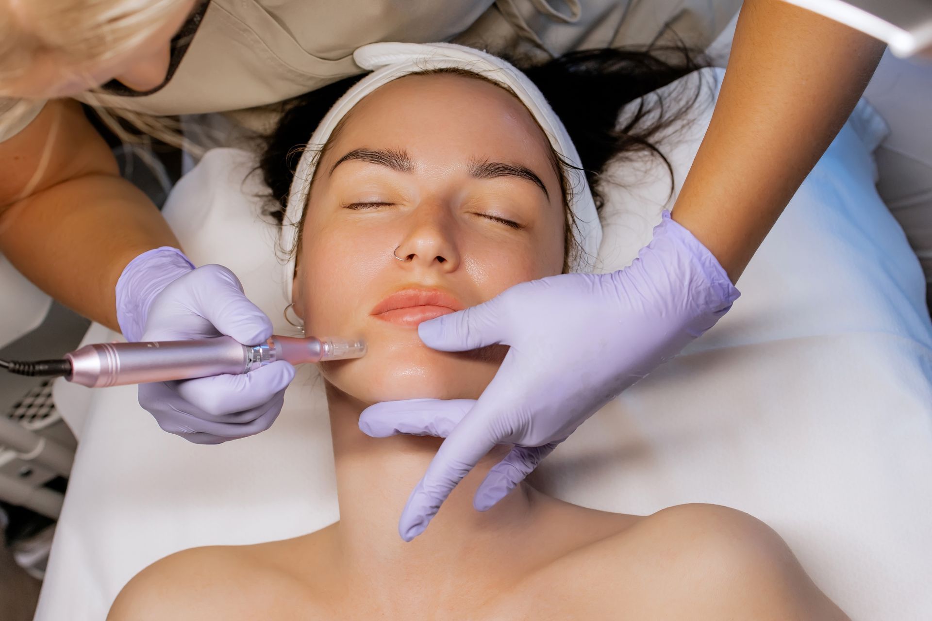 Person receiving lip micro-pigmentation. Technician in gloves holds a pen-like device to the client's lips.
