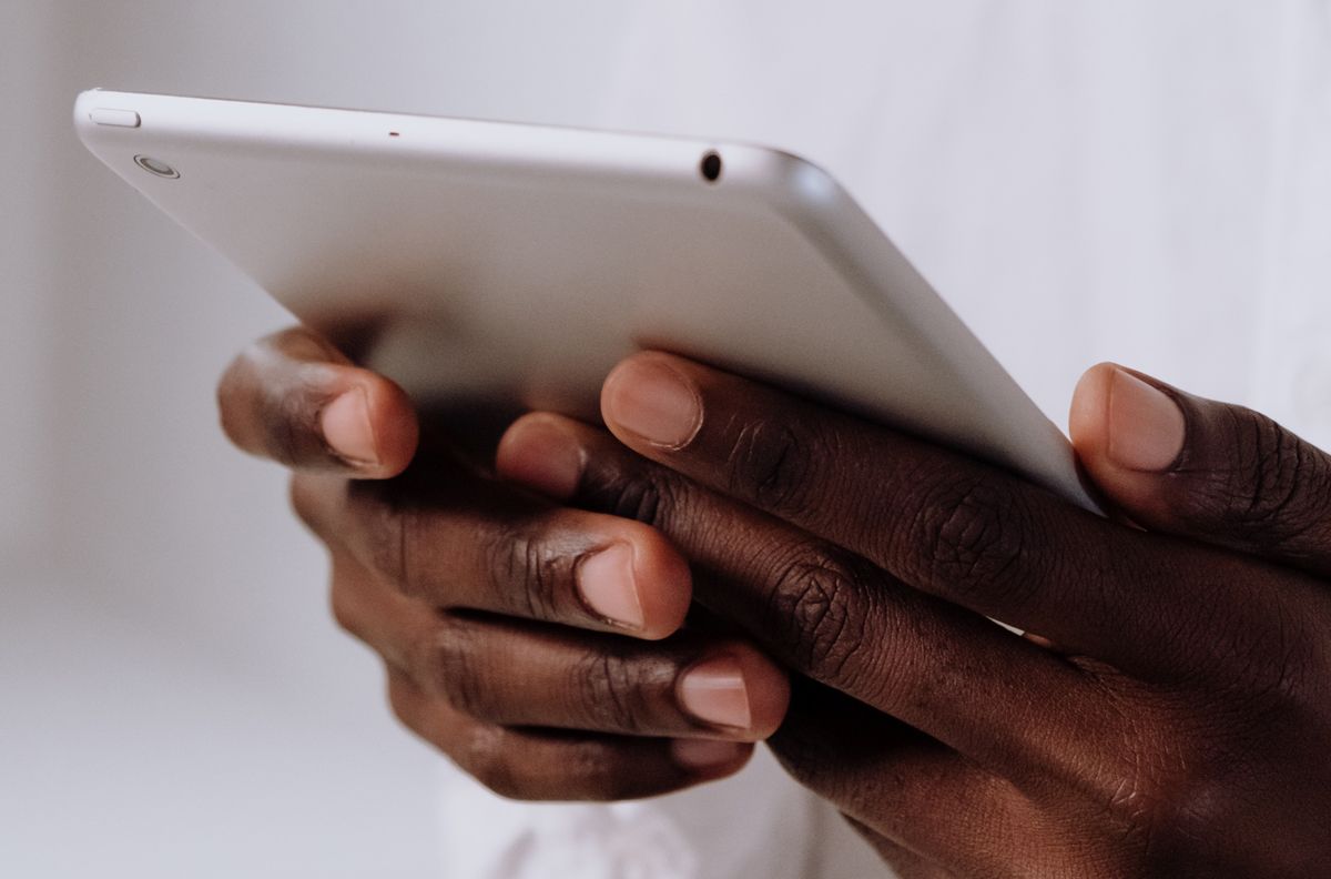 Hands of a Black person holding a silver tablet; close-up.