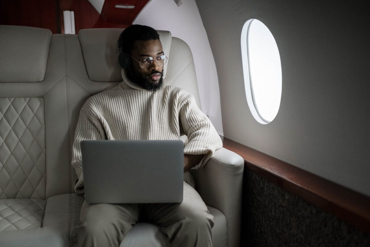 Man working on laptop inside a private jet, looking out the window.