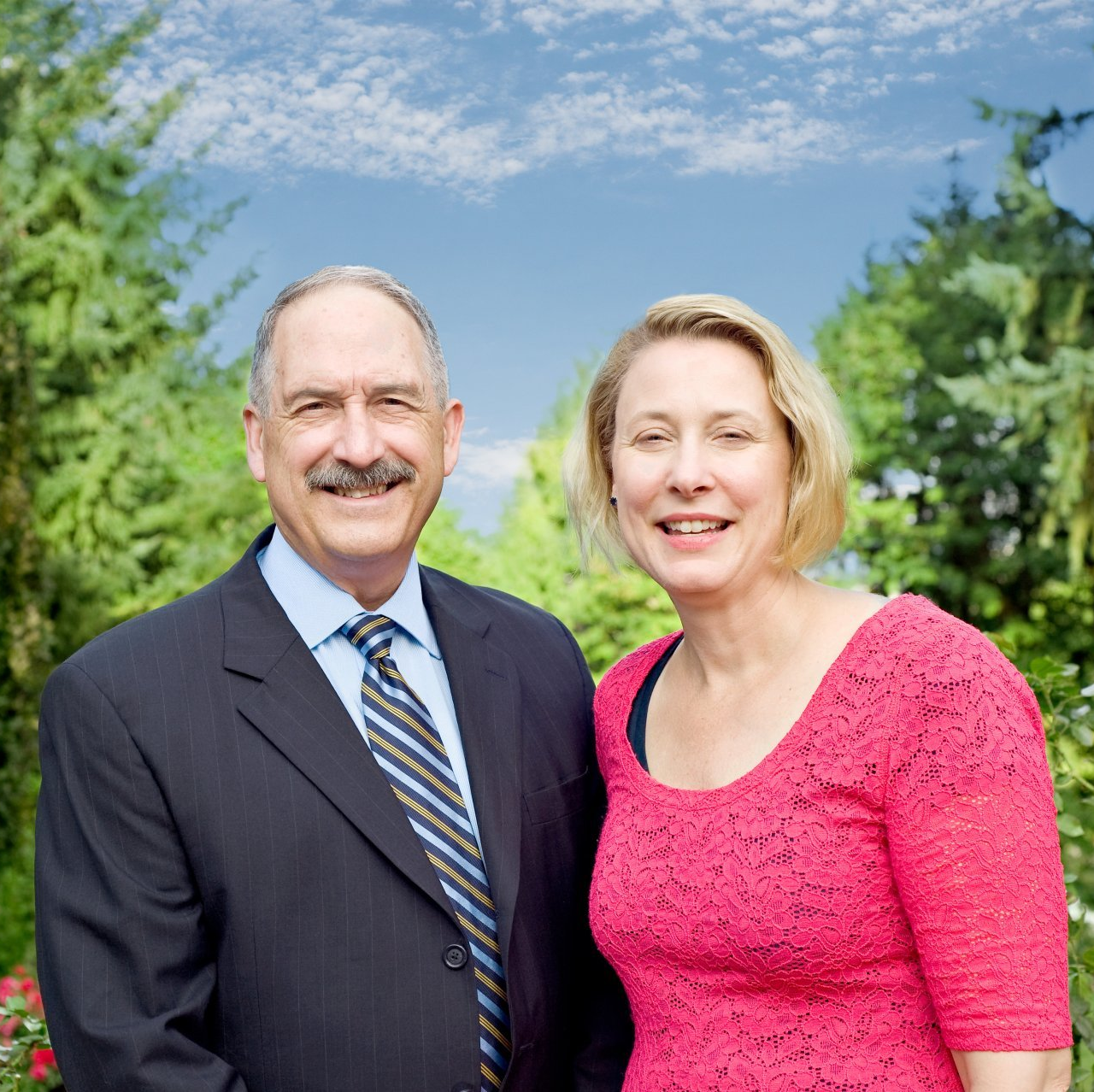 Smiling couple standing outdoors in front of trees and a blue sky