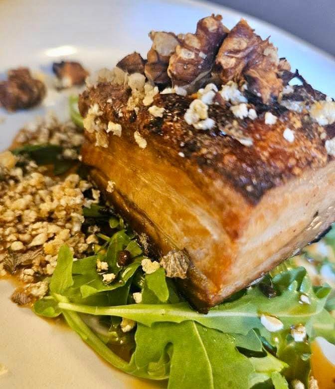 Roasted pork belly with walnuts and arugula on a white plate. Gourmet menu at the Boot & Shoe, Waterfoot