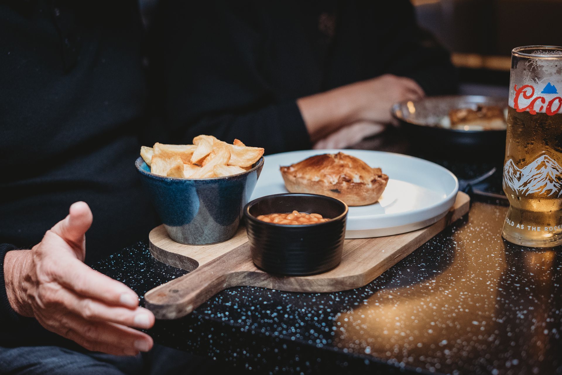 Food tray with pie, fries, and sauce, next to a beer, at a table. Food at the Boot & Shoe, Waterfoot, Rossendale
