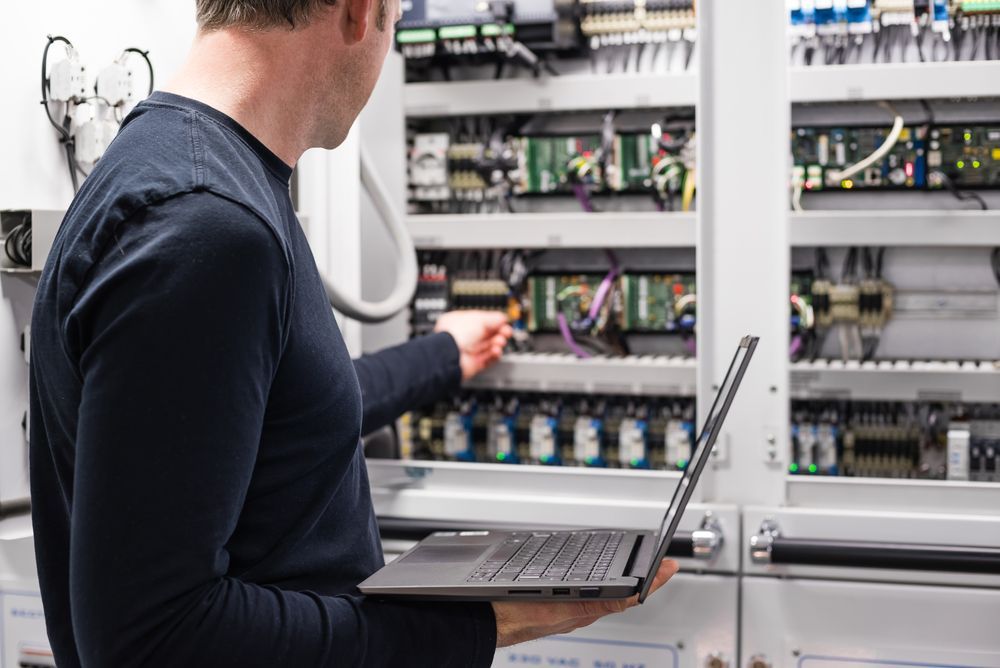 Man in Dark Shirt Working on an Electrical Panel With a Laptop — CKS Electrical and Air Conditioning in Alice Springs, NT