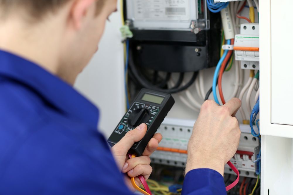 Electrician in Blue Overalls Using a Multimeter — CKS Electrical and Air Conditioning in Ciccone, NT