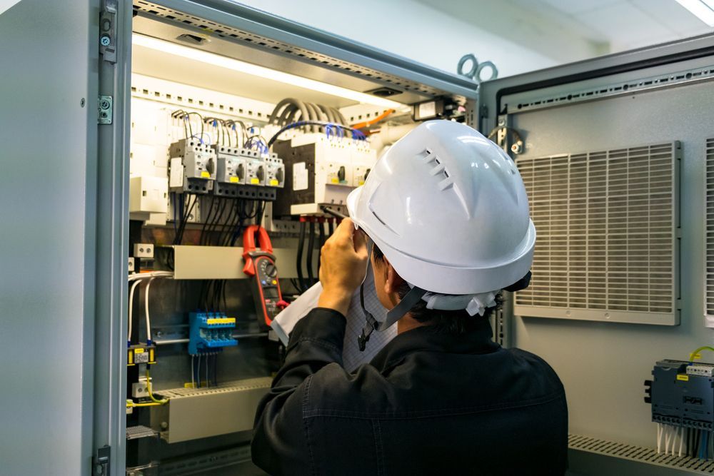an Electrician Wearing a Hard Hat Examines Electrical Wiring — CKS Electrical and Air Conditioning in Alice Springs, NT