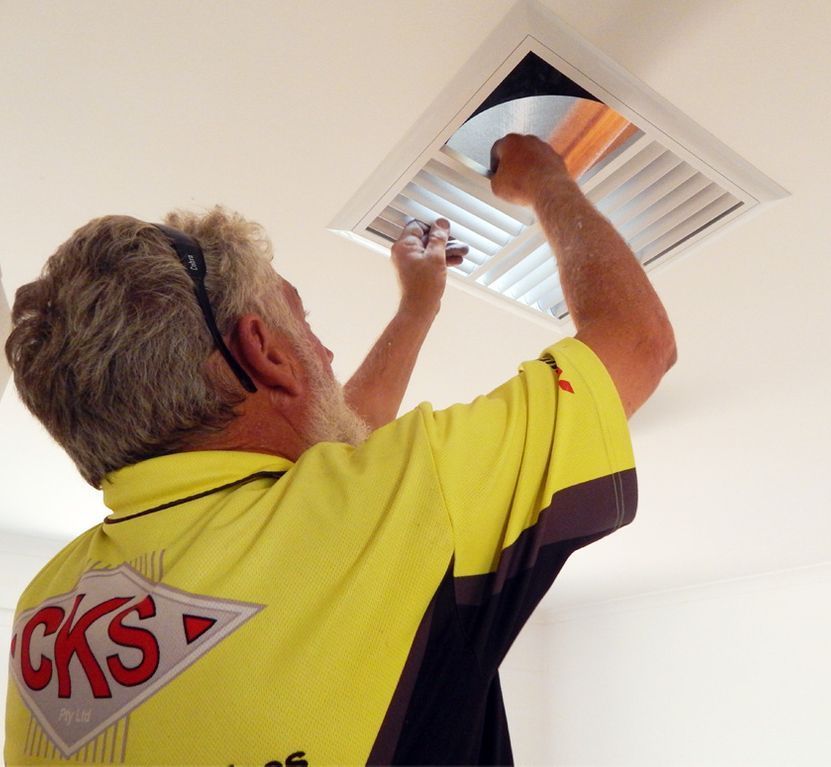 A Man in a Yellow Shirt is Installing a Vent Cover — CKS Electrical and Air Conditioning in Ciccone, NT