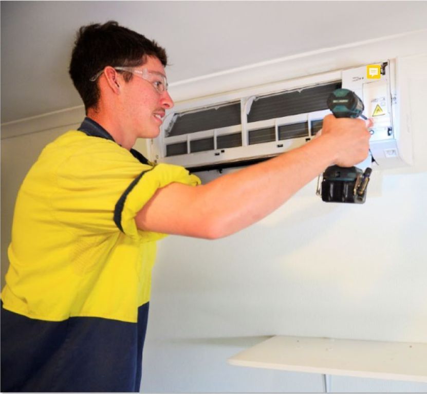 Man in Work Clothes Using a Drill to Service an Air Conditioning Unit — CKS Electrical and Air Conditioning in Ciccone, NT