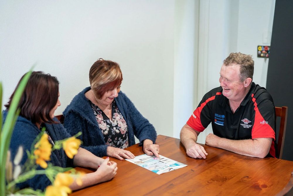 Three People Seated Around a Wooden Table, Looking at a Paper — CKS Electrical and Air Conditioning in Ciccone, NT