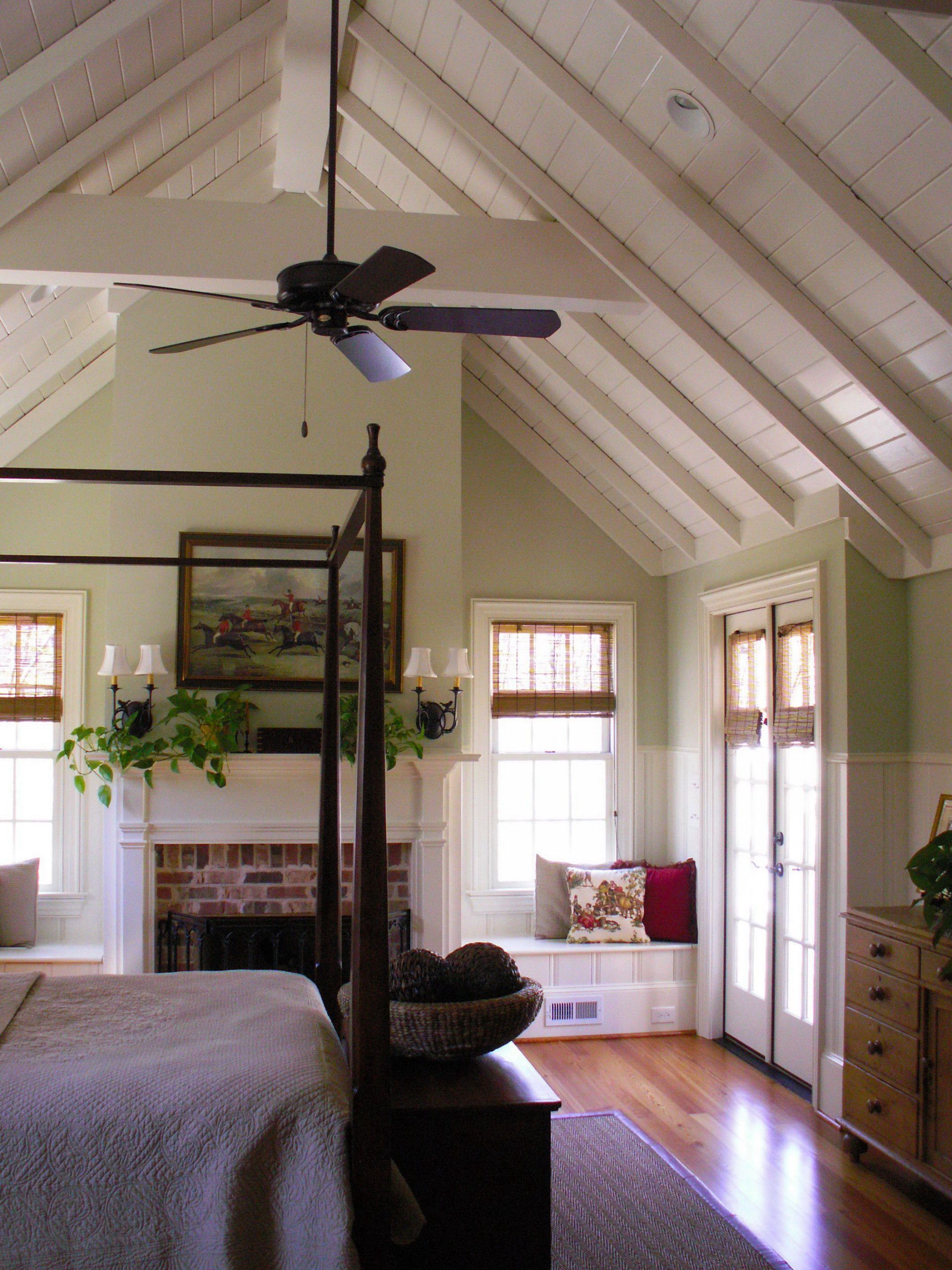 Bedroom with high, white-beamed ceiling, four-poster bed, fireplace, and windows with light green walls.