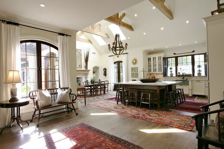 Spacious kitchen with exposed beams, an island, and a dining area, featuring warm lighting, and Persian rugs.