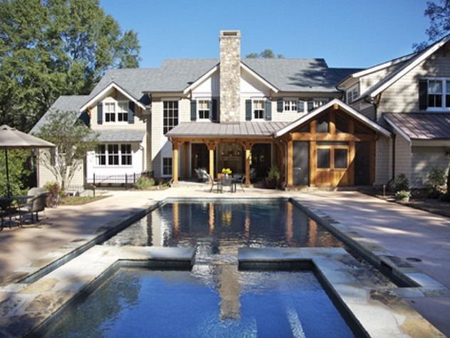 Large home with pool. Light-colored house, gray roof, stone chimney, wooden porch and pool with blue water.