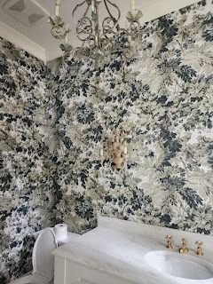 Bathroom with floral wallpaper, white sink, gold fixtures, and ornate chandelier.