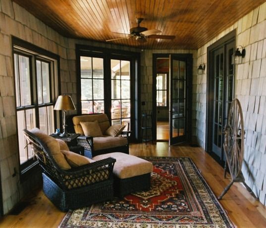 Sunroom with wicker furniture, red rug, wood ceiling, and large windows.