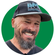 Smiling man in a black cap and shirt against a green background