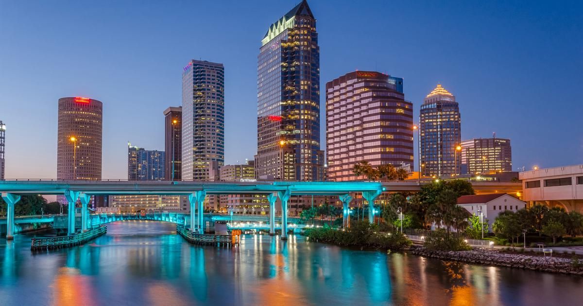 Tampa, Florida skyline at dusk, reflected in the water. Skyscrapers, bridges, and city lights glow.