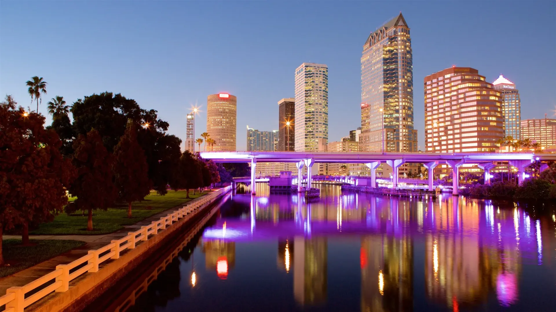Tampa, Florida skyline reflecting in the water at dusk with lit bridges and buildings.