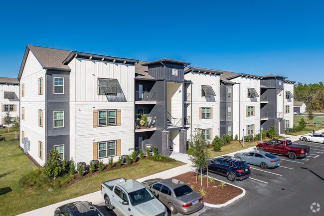 Exterior of modern apartment building with parking lot and cars under a clear blue sky.