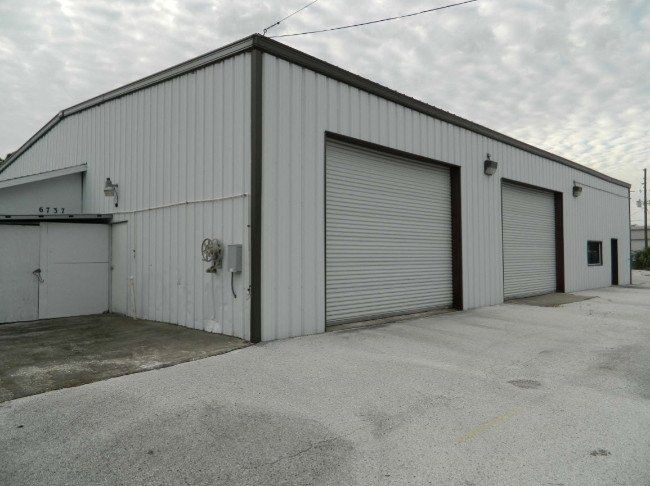A white metal industrial building with two large roll-up doors and a smaller side entrance under a cloudy sky.