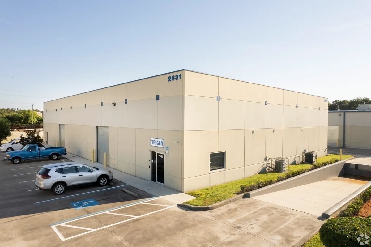 Beige commercial warehouse building with parked cars and a wheelchair-accessible ramp at the entrance