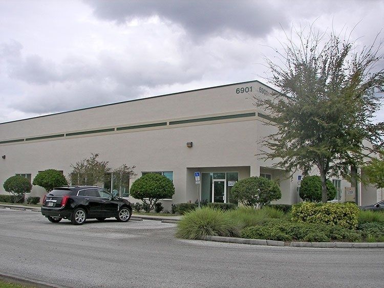 Industrial building exterior with parked SUV, shrubs, and cloudy sky