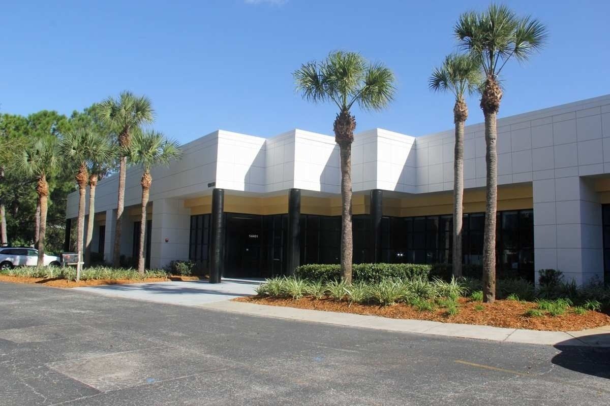 Modern white commercial building with palm trees and a paved parking lot