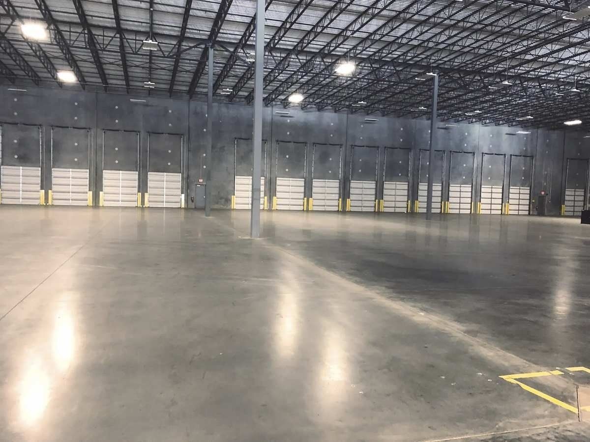 Empty warehouse interior with polished concrete floor, metal roof beams, and loading dock doors.