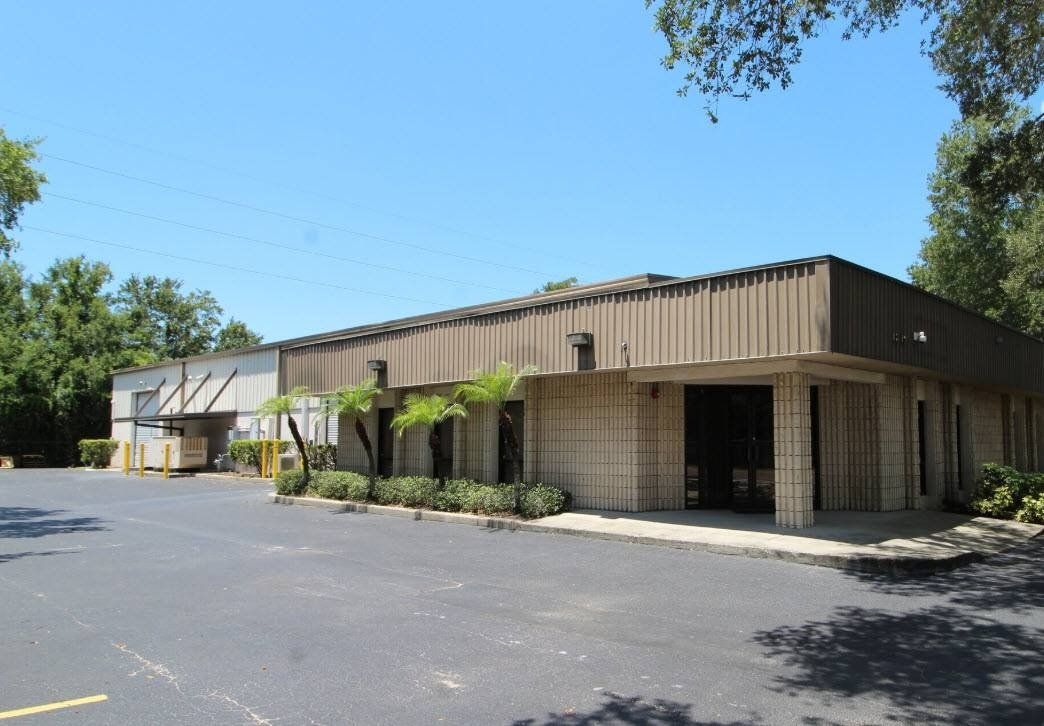 Low, brown commercial building with covered walkway and empty parking lot under blue sky