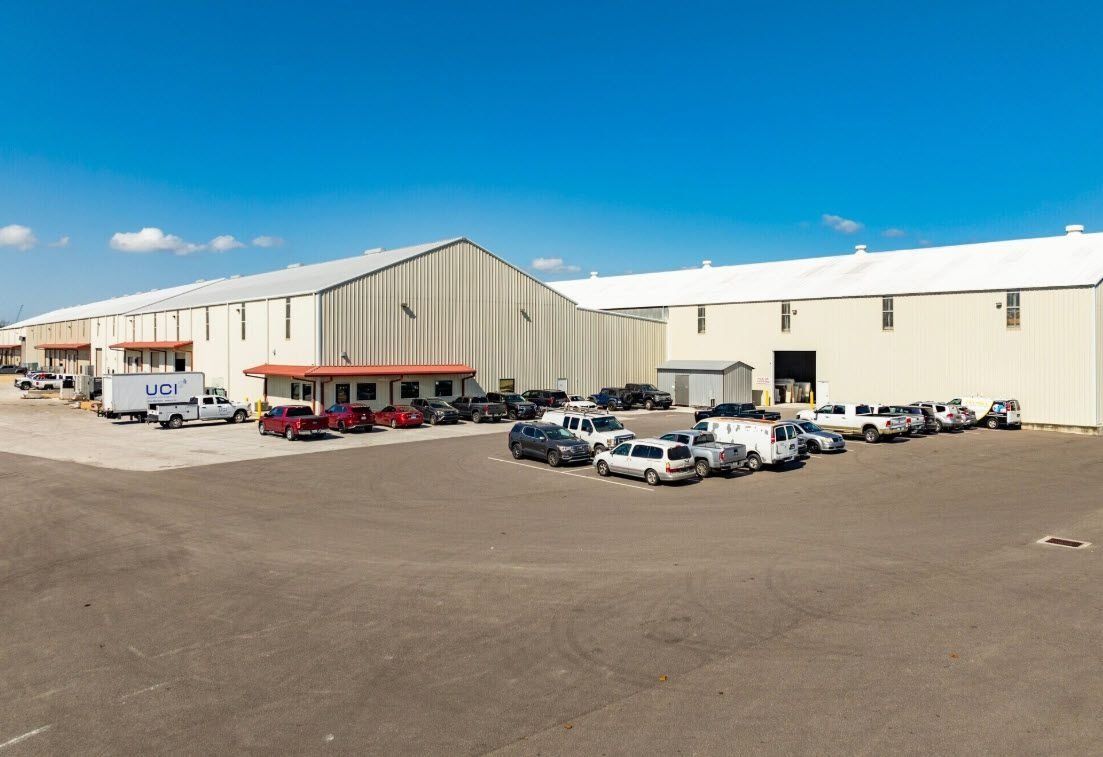 Large warehouse building with parked trucks and cars in a sunny industrial lot