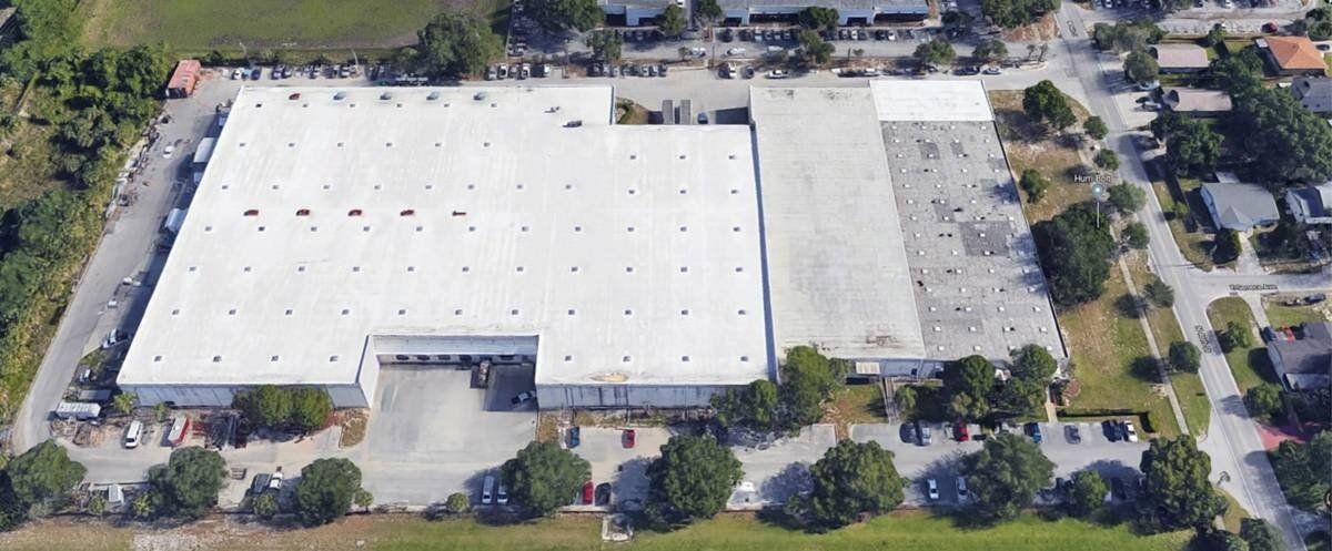 Aerial view of a large white-roofed building with parking lots and trees around it