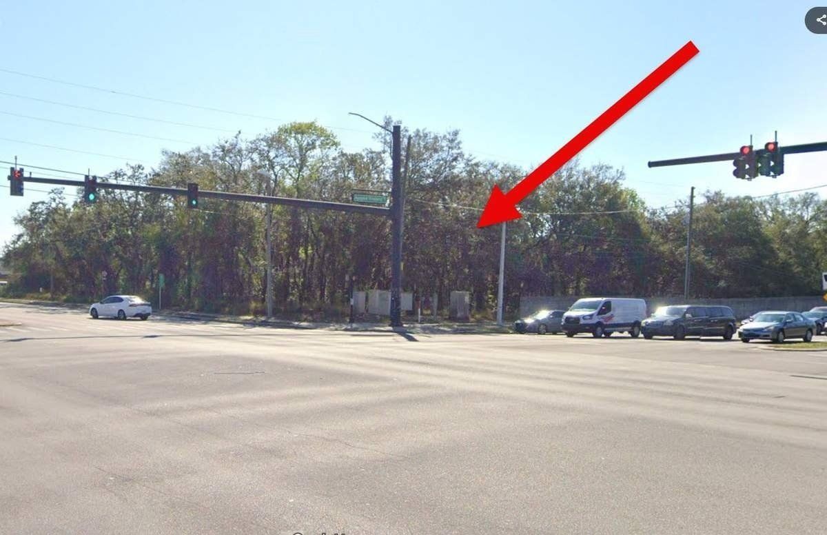 Busy intersection with traffic lights and cars; red arrow points to a roadside utility box near trees.