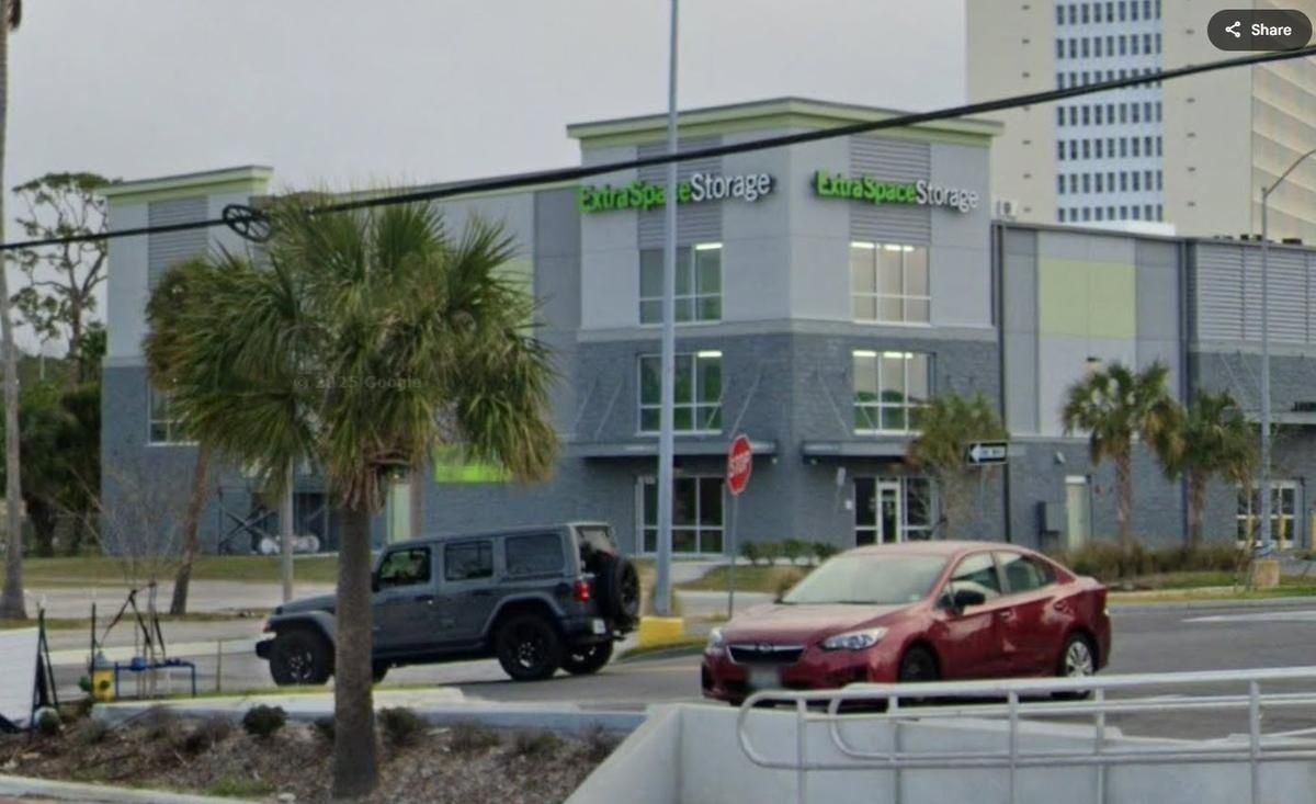 Two parked cars outside a modern gray office building with green signage and palm trees.