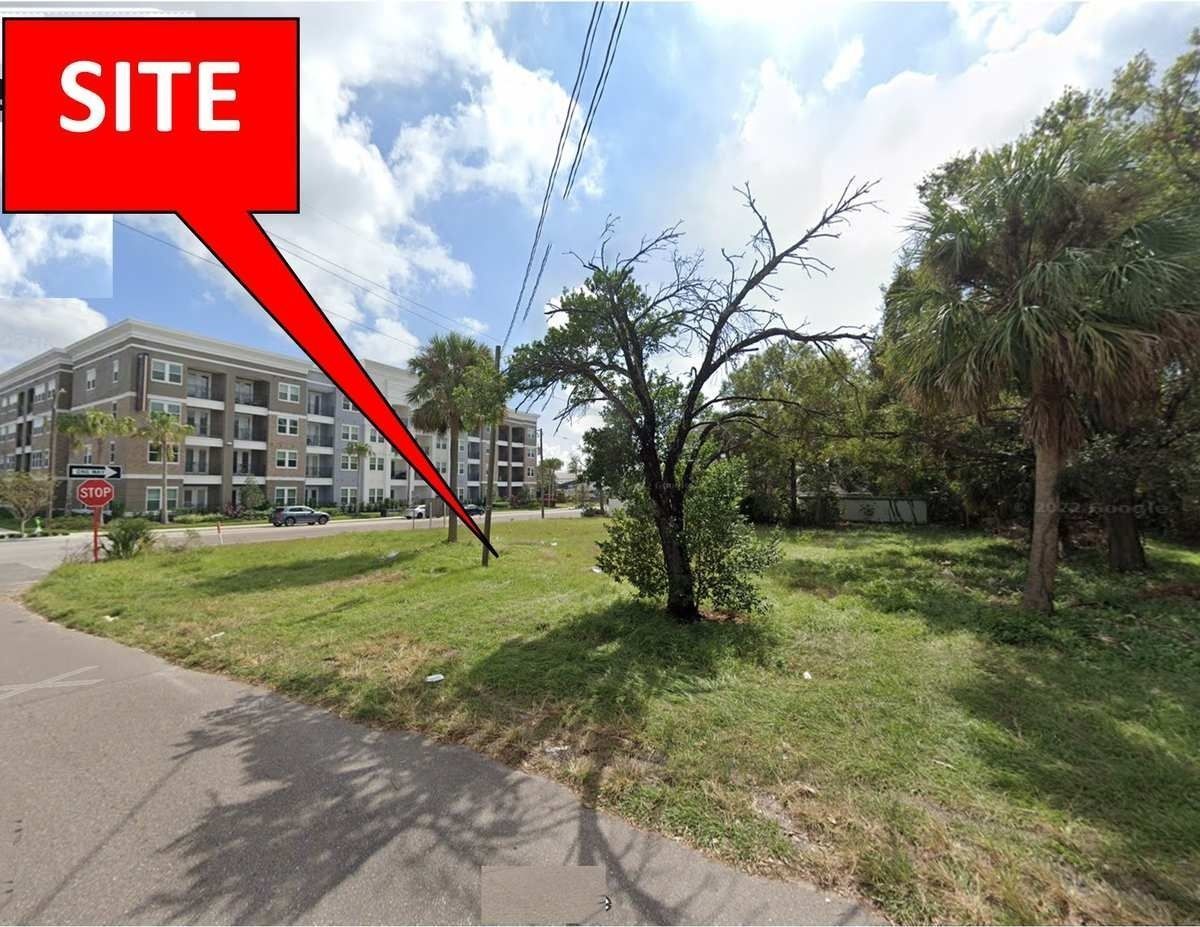 Open grassy lot beside a road and apartment building, marked with a red “SITE” callout.