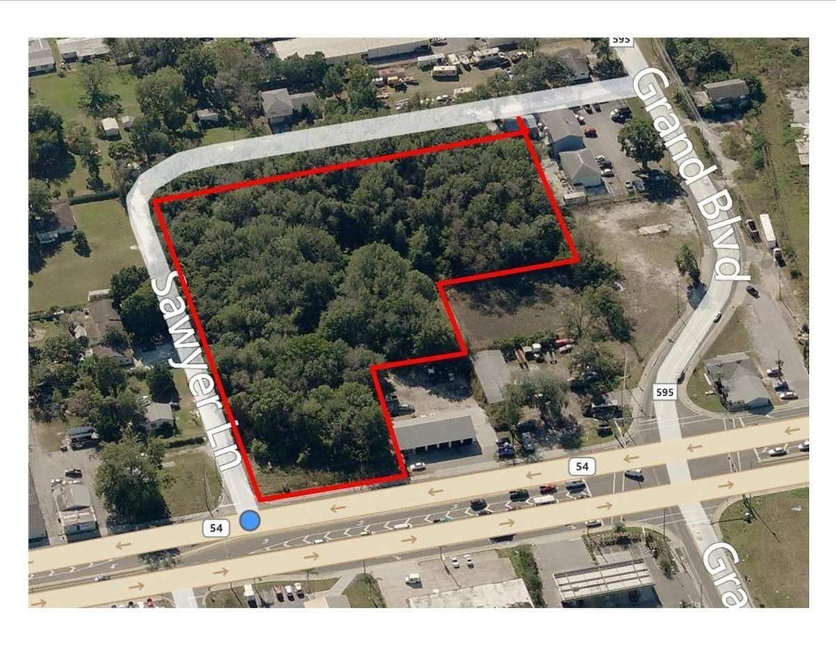 Aerial view of a vacant plot of land bordered by a white dotted line, next to a