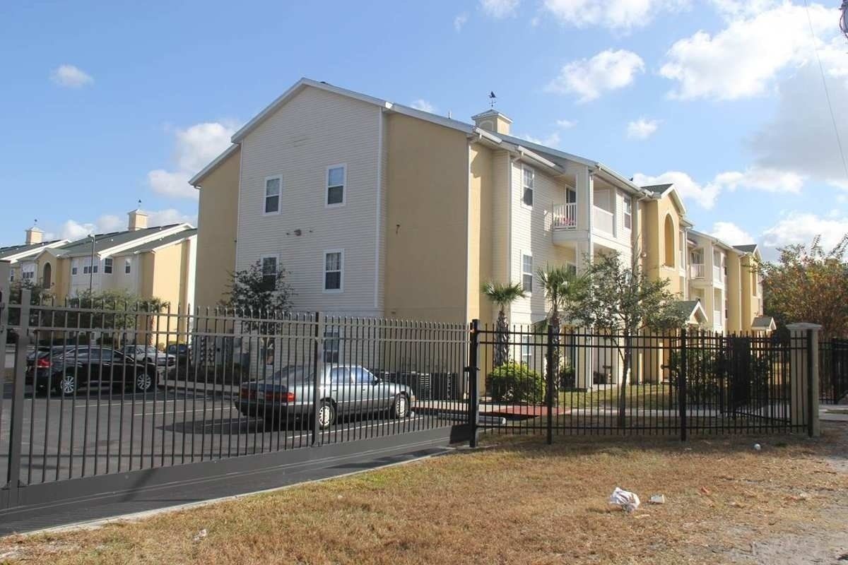 Apartment buildings behind a black metal fence under a partly cloudy sky