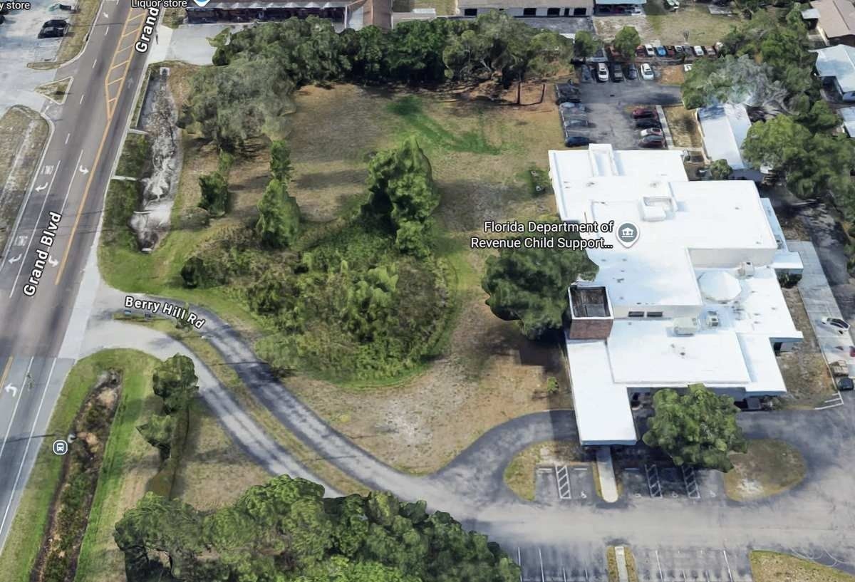 Aerial view of a white building beside a grassy lot and winding driveway near a road.