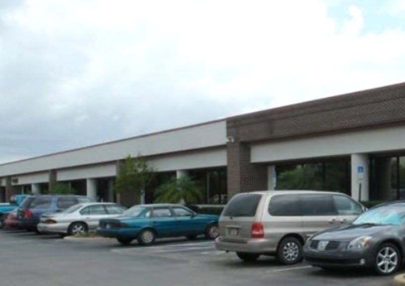 Strip mall storefront with parked cars in a lot under a cloudy sky