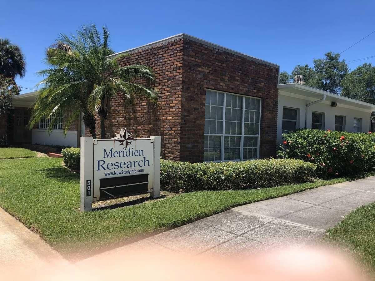 Brick office building with a sign reading “Merriam Research” beside a sidewalk and palm trees
